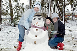 A lesbian couple with a child posing with a snowman in a forest.