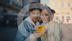 Lesbian couple standing in the city centre, choosing the pictures , scrolling social media, feeling happy together