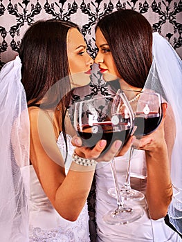 Lesbian couples in wedding bridal dress kissing and drinking red wine.