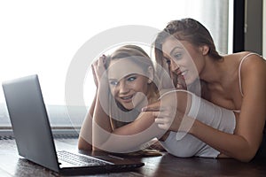 Lesbian domestic couple on floor at laptop, pointing to screen photo