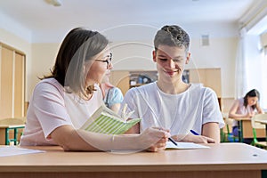 Lesson in class of high school students, female teacher sitting at desk with student