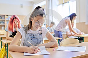 Lesson in class of teenage children, in front girl sitting at desk writing in notebook