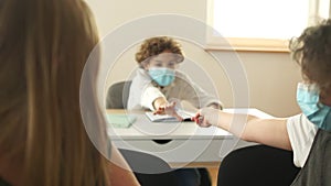 Lesson in the classroom in high school. Masked children in the classroom, girl gives a pen to a boy. Post-quarantine