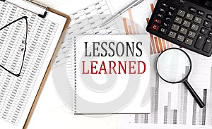 LESSONS LEARNED text on notebook with clipboard and calculator on a chart background