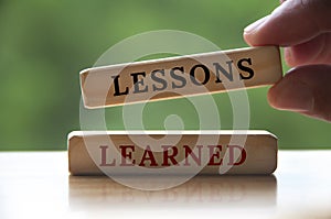 Lessons learned text on wooden blocks with hand holding and blurred nature background. Learning concept