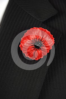 Lest We Forget Red Poppy Lapel Pin Badge on black suit - vertical.