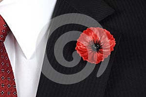 Lest We Forget Red Poppy Lapel Pin Badge on man's black suit.