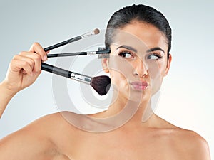 Let the beautifying begin. Studio shot of a beautiful young woman holding makeup brushes against a gray background.