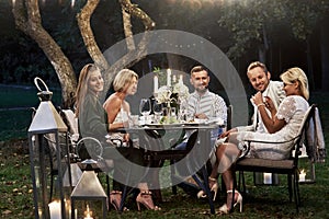 Let candles burn that night. Group of adult friends have a rest and conversation in the backyard of restaurant at