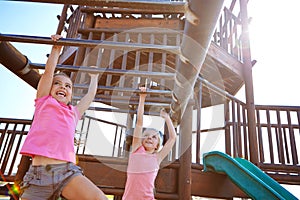 Let children be children for as long as possible. two little girls hanging on the monkey bars at the playground.