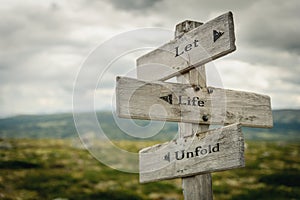 let life unfold text engraved on old wooden signpost outdoors in nature photo
