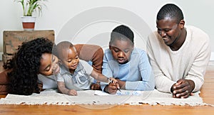 Let me help you. a two young parents lying on the living room floor with their children and watching them draw.