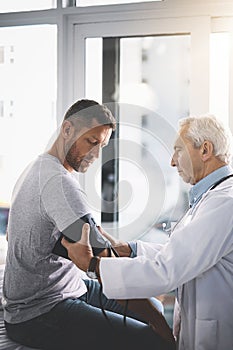 Let me just get your blood pressure. a senior doctor giving his male patient a thorough checkup during his consultation.