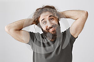 Let me scrape hair in ponytail. Portrait of funny handsome arabian guy with beard holding hands behind head and smiling
