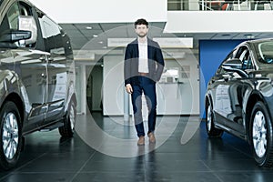 Let me show our new model. Handsome young classic car salesman standing at the dealership near new cars