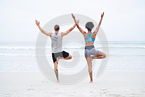 Let no storm overpower your soul. Rearview shot of a young man and woman practising yoga together at the beach.