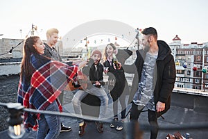 Let`s drink and have fun. Five young friends have party with beer and guitar at the rooftop