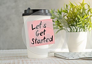 Let\'s Get Started Text Written on Sticky Paper on Coffee Gass on Office Desk