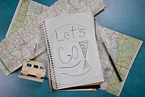 Let\'s Go! Handwritten on spiral notebook laying on old folded road maps lay flat travel themed background