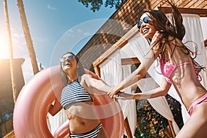 Let& x27;s go with me! Two playful young women in swimwear are holding hands and smiling while one of them carrying