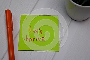 Let`s Thrive write on sticky note isolated on wooden table