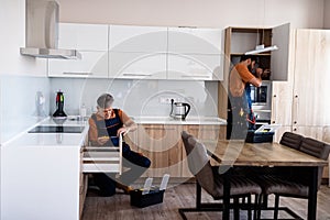 Let us work. Full length shot of two handymen, workers in uniform assembling kitchen cupboard, cabinet using screwdriver