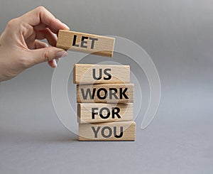 Let us work for you symbol. Wooden blocks with words Let us work for you. Beautiful grey background. Businessman hand. Business