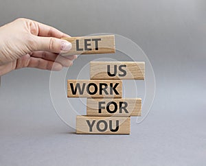 Let us work for you symbol. Wooden blocks with words Let us work for you. Beautiful grey background. Businessman hand. Business