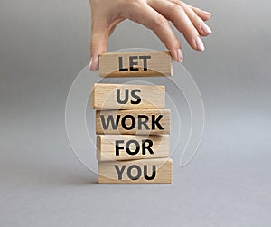 Let us work for you symbol. Wooden blocks with words Let us work for you. Beautiful grey background. Businessman hand. Business