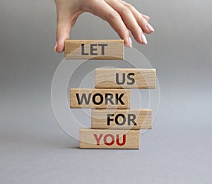 Let us work for you symbol. Wooden blocks with words Let us work for you. Beautiful grey background. Businessman hand. Business