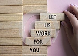 Let us work for you symbol. Wooden blocks with words Let us work for you. Beautiful pink background. Businessman hand. Business