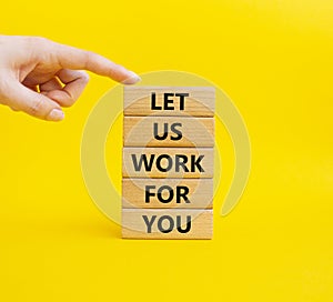 Let us work for you symbol. Wooden blocks with words Let us work for you. Beautiful yellow background. Businessman hand. Business