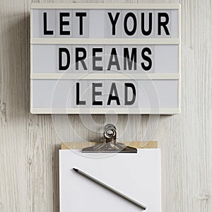 `Let your dreams lead` on a modern board, clipboard with blank sheet of paper on a white wooden surface, top view. Flat lay,