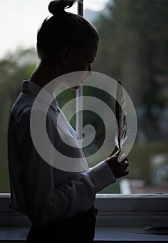 Let your imagination take flight. A young woman standing by a window holding a feather.