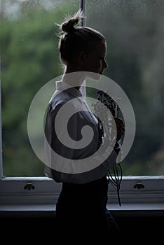 Let your imagination take flight. A young woman standing by a window holding flowers.