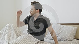 Lethargic man waking up in morning slowly. Handsome guy sitting on bed.