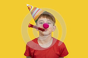 Lets celebrate! Boy in festive hat and clown nose on yellow background. Childrens party