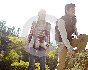 Lets climb up here. A happy young couple hiking through nature together.