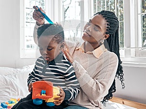 Lets comb this hair. an attractive young woman combing her sons hair while sitting on a bed at home.