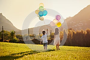 Lets get carried away together. Rearview shot of two cute little siblings holding balloons while walking outside.