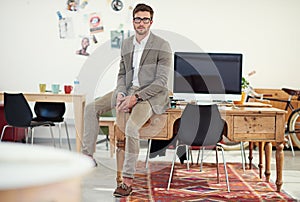 Lets get to work. Portrait of a casually-dressed young man sitting on his desk in an office.