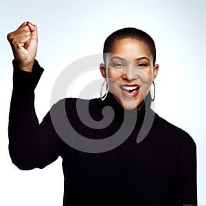 Lets go ladies. Studio shot of an attractive young woman posing with her arm raised and fist clinched against a grey photo