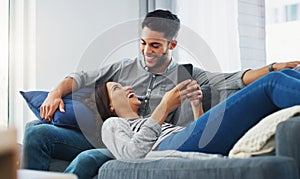 Lets go through our pictures. an affectionate young couple lounging on the sofa while using a cellphone in their living
