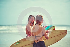 Lets hit the waves. a young couple walking on the beach with their surfboards.