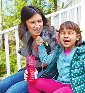 Lets make the best of the sunshine today. a mother watching her daughter blow bubbles outside.