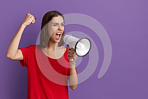 Lets make the world great. We are against this policy. Confident pretty brunette girl in red t-shirt screams in megaphone. Protest