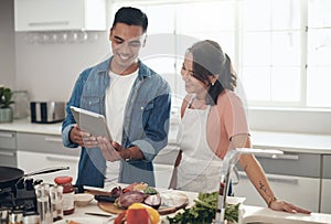 Lets read the recipe together. a young couple using a digital tablet while cooking together at home.