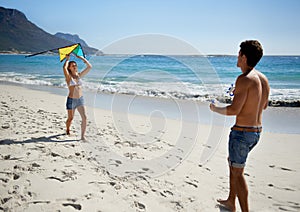 Lets see how high we can get it. A fun-loving young couple playing with a kite while enjoying a day on the beach.