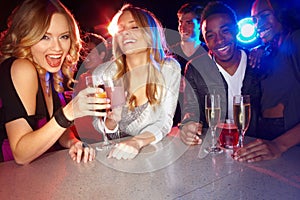 Lets see where the night takes us. A group of friends smiling at the camera while they enjoy drinks in a nightclub.
