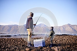 Lets throw it in the deep. Shot of a father and son standing with their fishing gear by the sea.